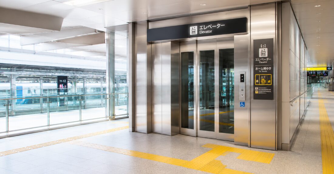新大阪駅の東改札奥に位置する、階段を回避して各フロアをフラットに繋ぐ大型エレベーターと点字ブロックの動線